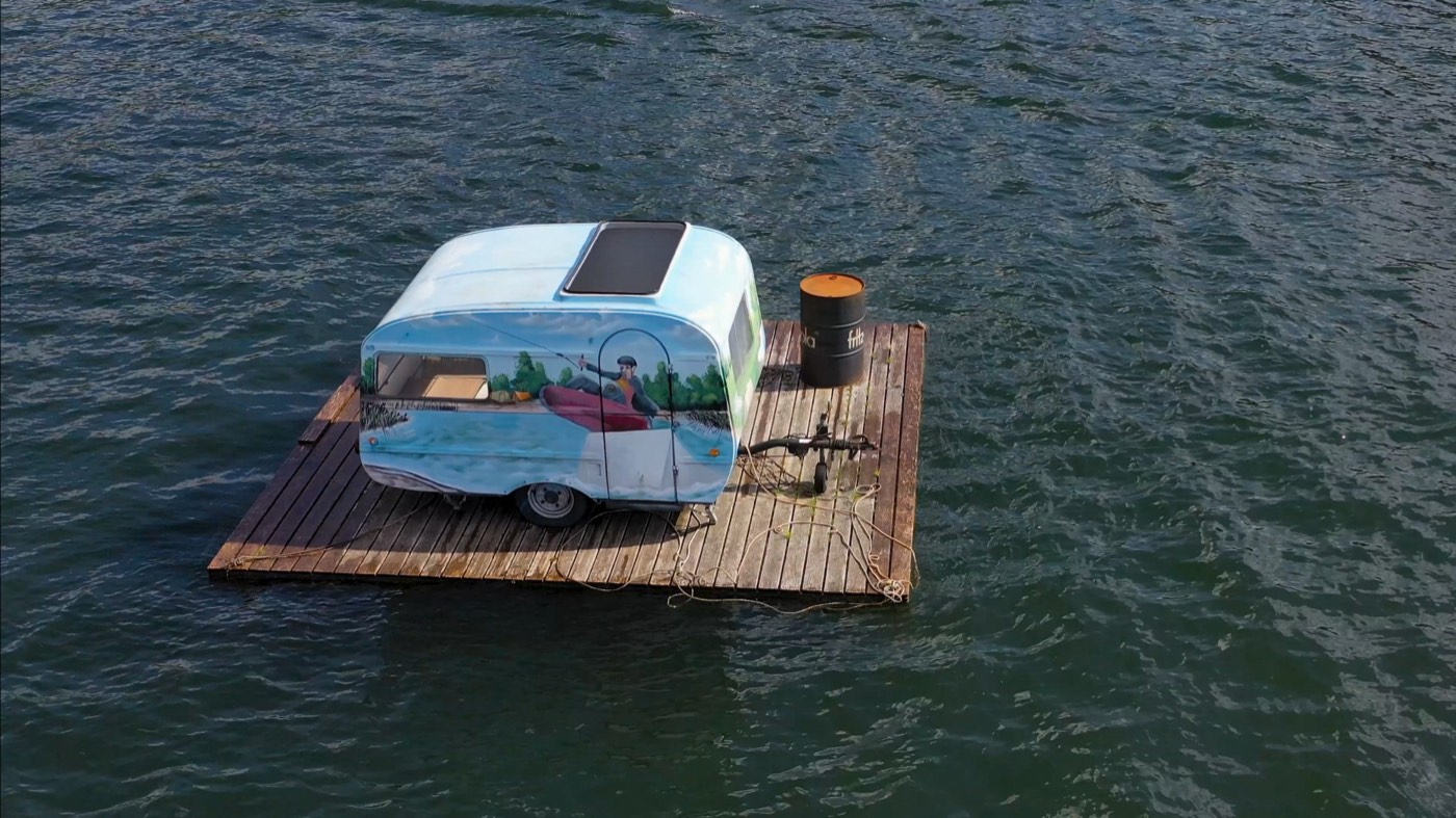Floating-Glamping: bemalter Wohnwagen auf einem Ponton im See
